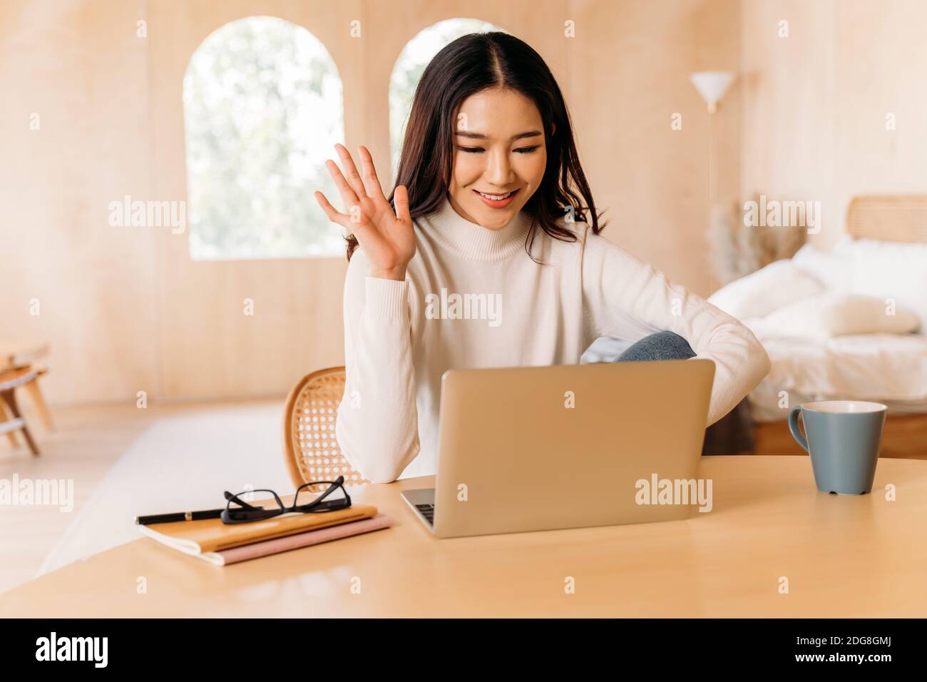 Junge Teenager asiatische Frau tragen Pullover mit hübschen Lächeln winken auf jemanden in Laptop in gemütlichen Zimmer. Glückliche und stilvolle Mädchen Videoanrufe und Konferenzen. Winter Business Portrait Lifestyle. Speicherplatz kopieren Stockfoto