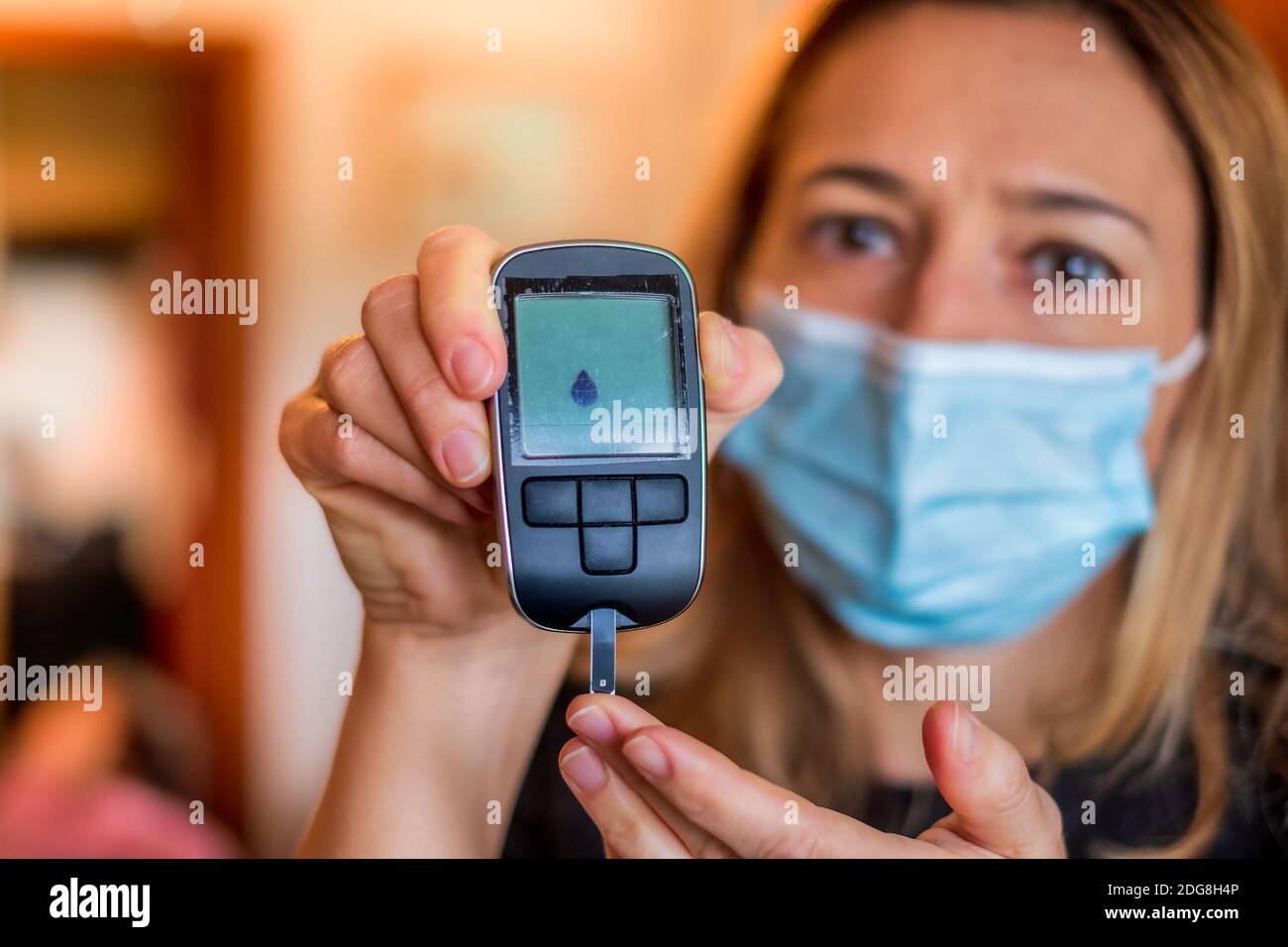 Glucometer-Gerät für Glukosetest mit tropftem Blut bei Diabetikern Patienten von der blonden Krankenschwester mit OP-Maske gehalten Stockfoto