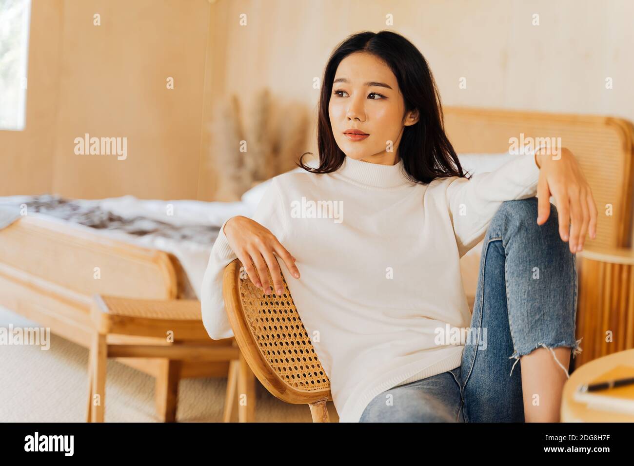 20s junge Teenager asiatische Frau trägt einen Pullover Blick weg in stilvollen gemütlichen Raum Hintergrund. Attraktive weibliche Modell posiert für Kamera auf Stuhl. Winter Portrait Mode Lifestyle. Platz für die Banner-Kopie Stockfoto