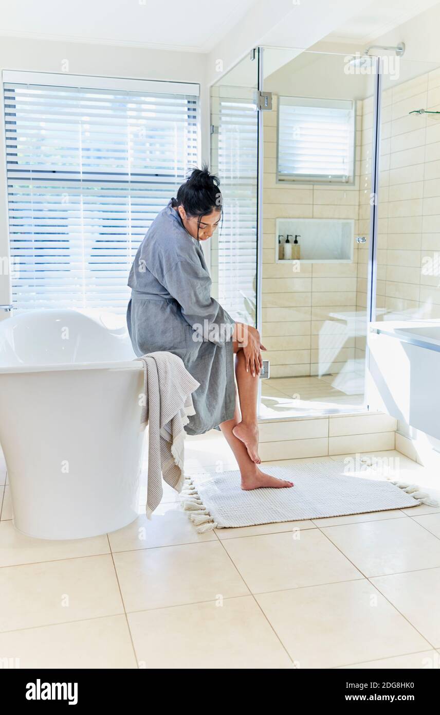 Frau im Bademantel berühren Bein in Hause Vitrine Innenbadezimmer Stockfoto
