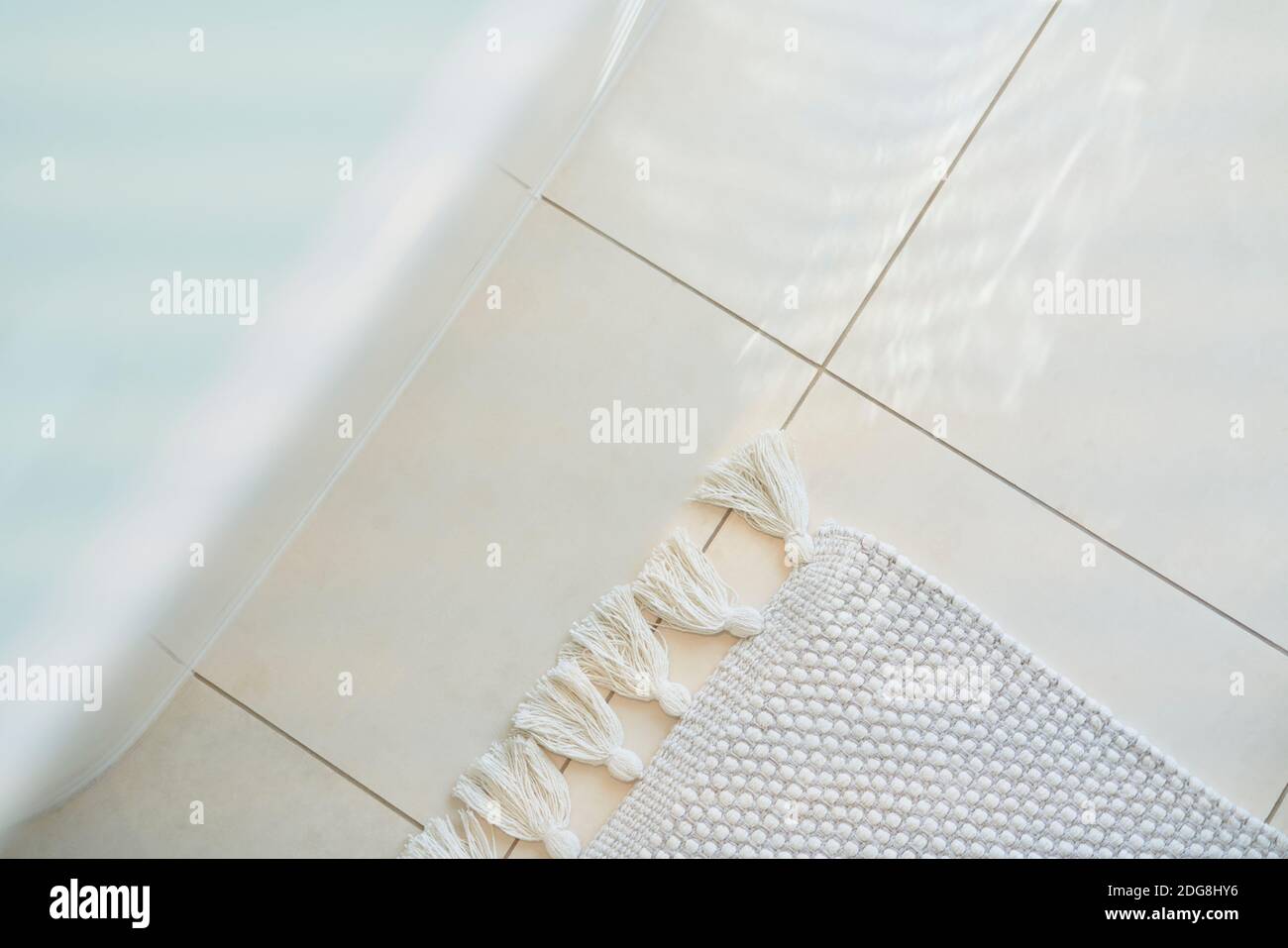 Fransenteppich auf weißem Fliesenboden unter der Badewanne im Badezimmer Stockfoto