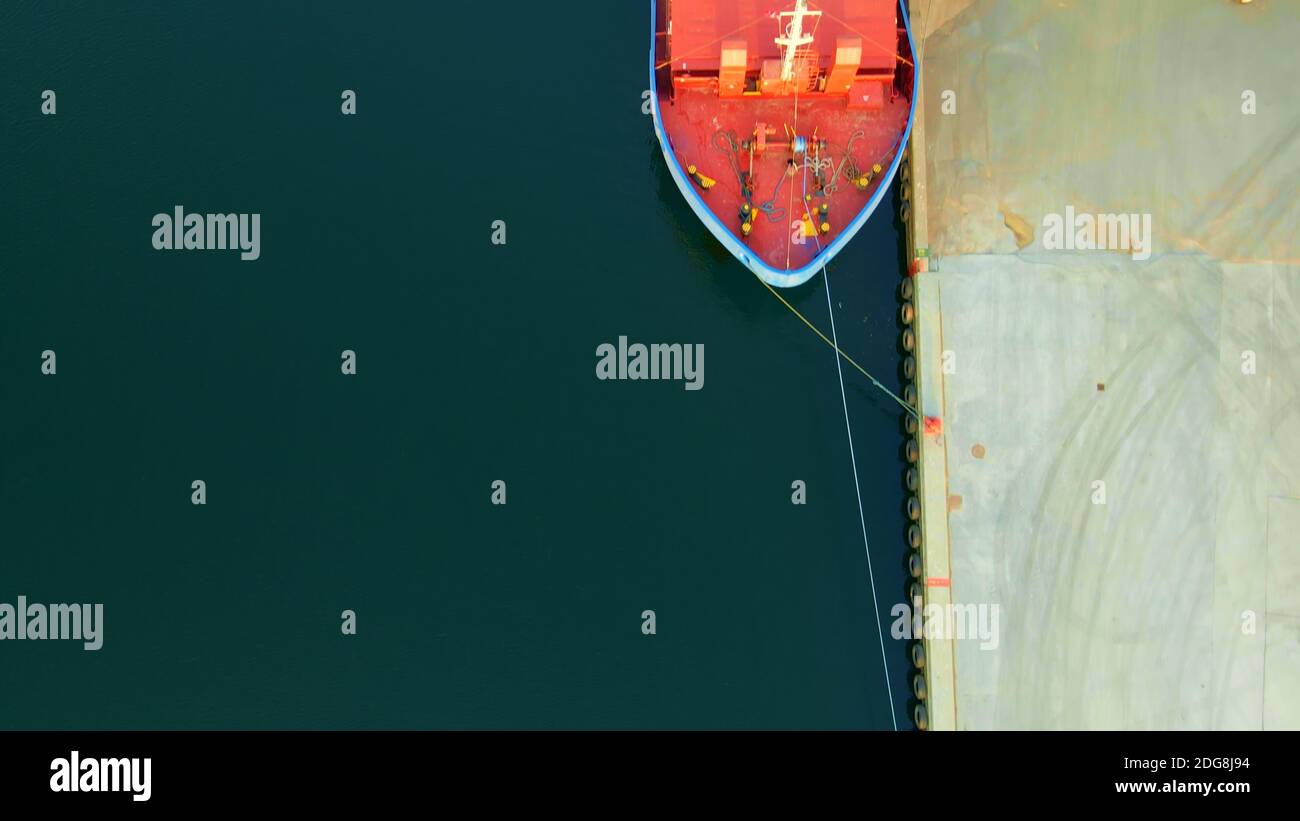 Bug eines Frachtschiffs im Hafen mit Anlegestellen, die das Schiff an den Schiffspollern auf dem Dock befestigen. Luftaufnahme. Stockfoto