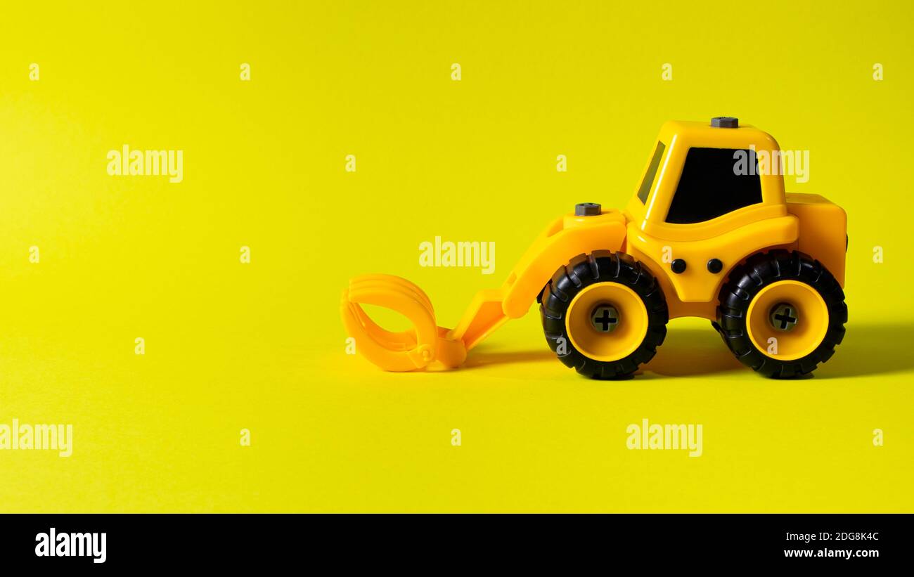 Kinderbaumaschine Holzlader auf gelbem Hintergrund. Traktor für den Jungen und Foto für den Spielwarenladen mit Platz für Textkopie Stockfoto