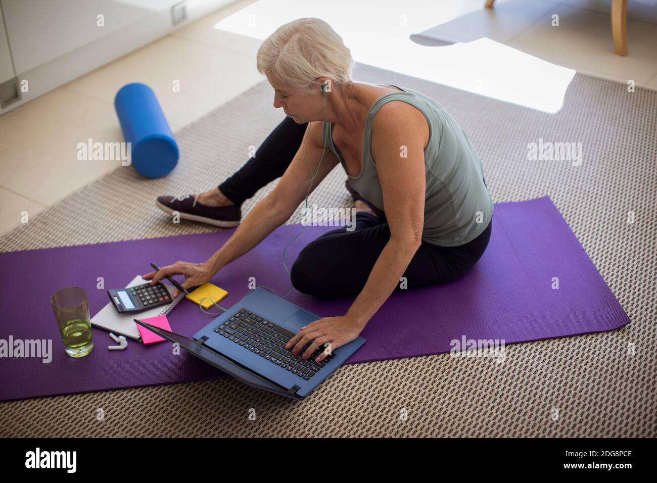 Ältere Frau, die Rechnungen bezahlt und am Laptop Yoga trainiert Mat Stockfoto