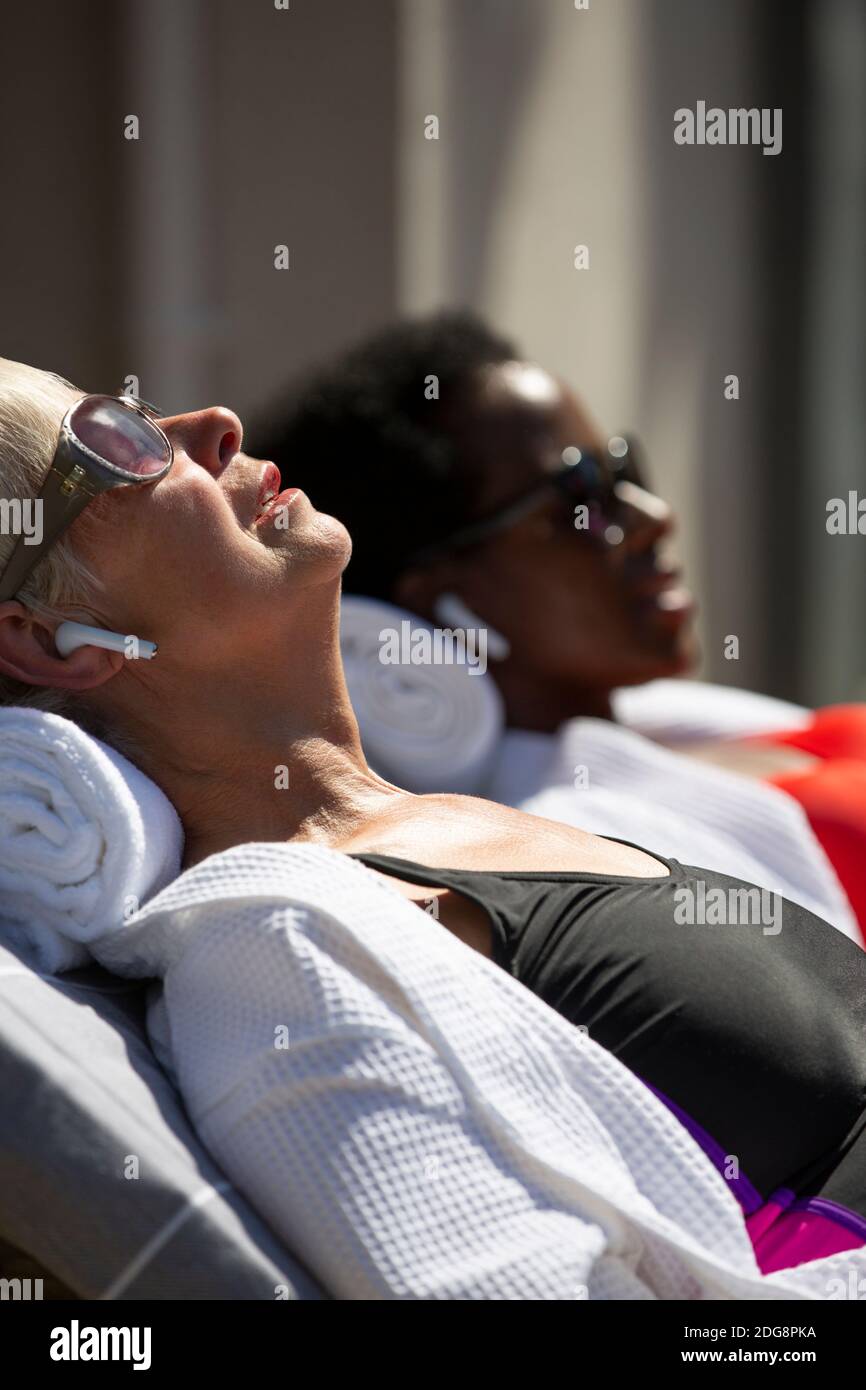 Ältere Frau mit Ohrhörern, Sonnenbaden auf der sonnigen Terrasse Stockfoto