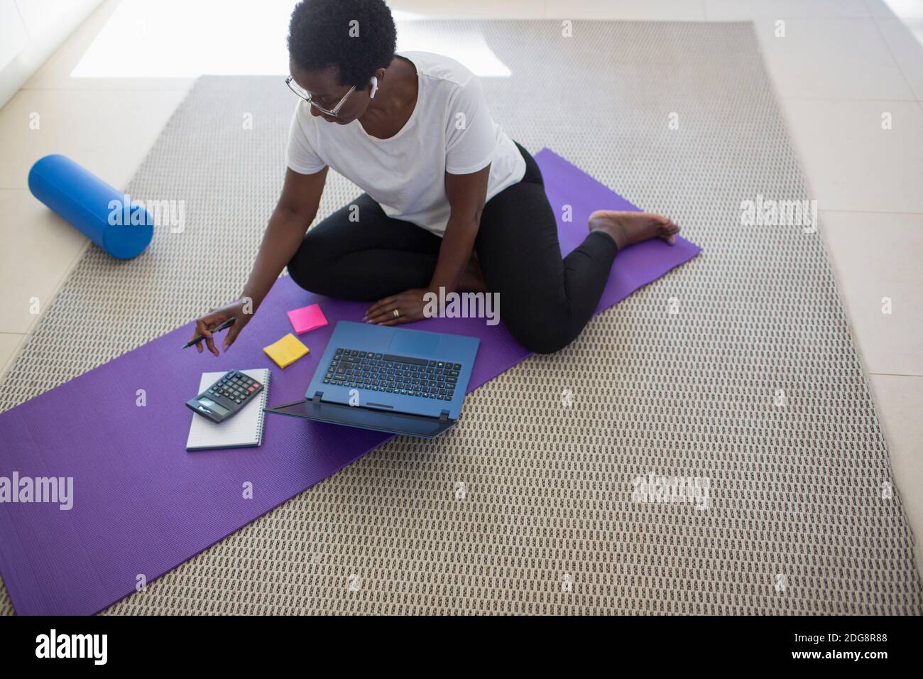 Reife Frau zahlt Rechnungen und arbeitet am Laptop auf Yoga Mat Stockfoto