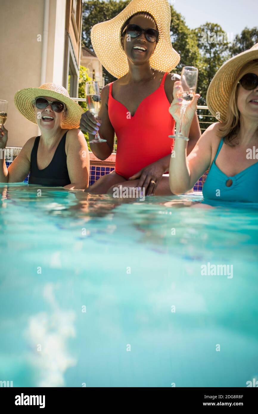 Glückliche ältere Freundinnen trinken Champagner im sonnigen Schwimmbad Stockfoto