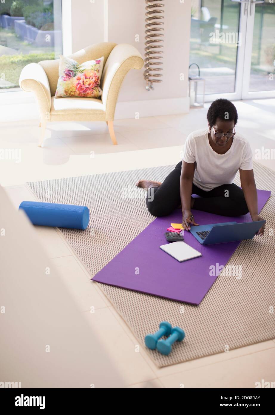 Reife Frau arbeitet am Laptop auf Yoga-Matte zu Hause Stockfoto