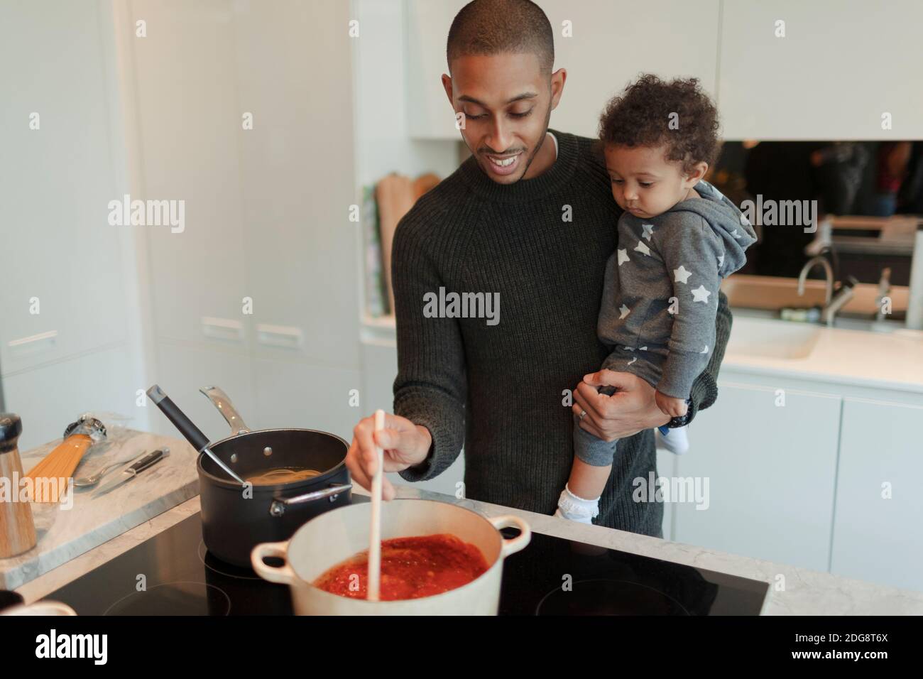 Glücklicher Vater hält Baby Tochter und Kochen Spaghetti am Herd Stockfoto