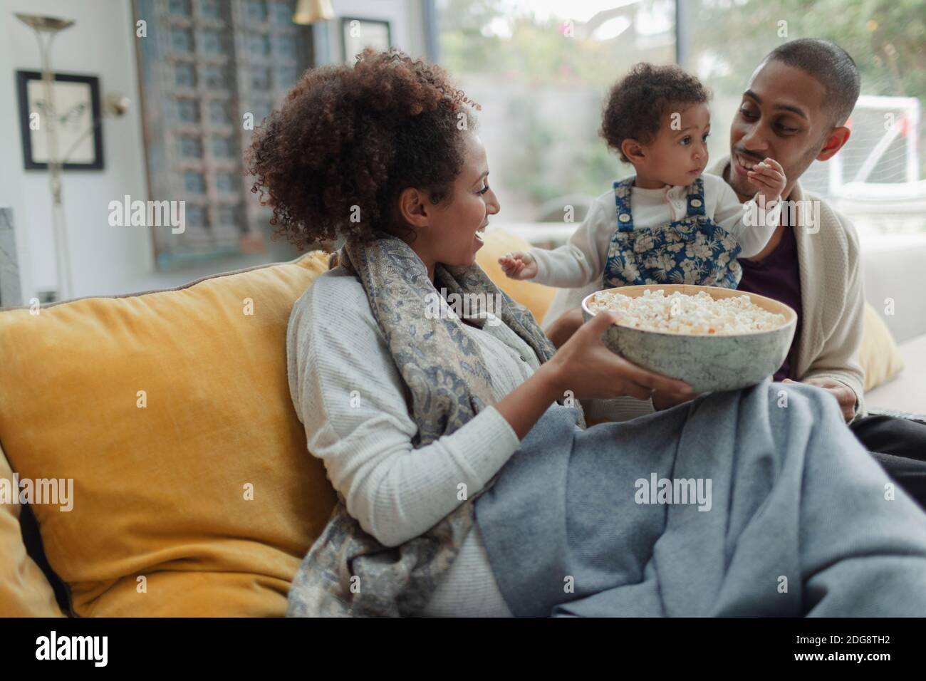 Glückliche Eltern und kleine Tochter, die mit Popcorn Fernsehen Sofa Stockfoto