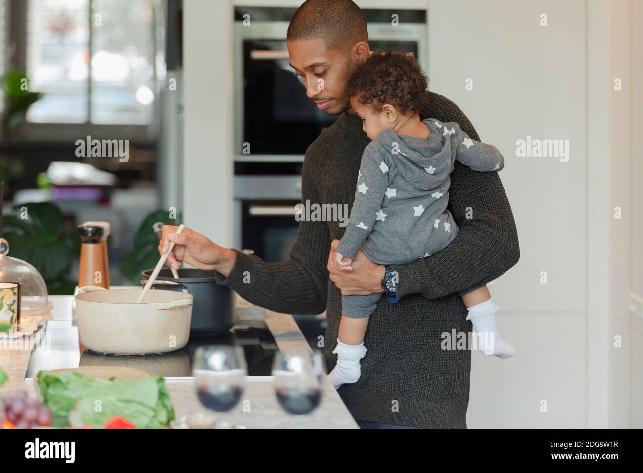 Vater hält Baby Tochter und Kochen Abendessen am Küchenherd Stockfoto