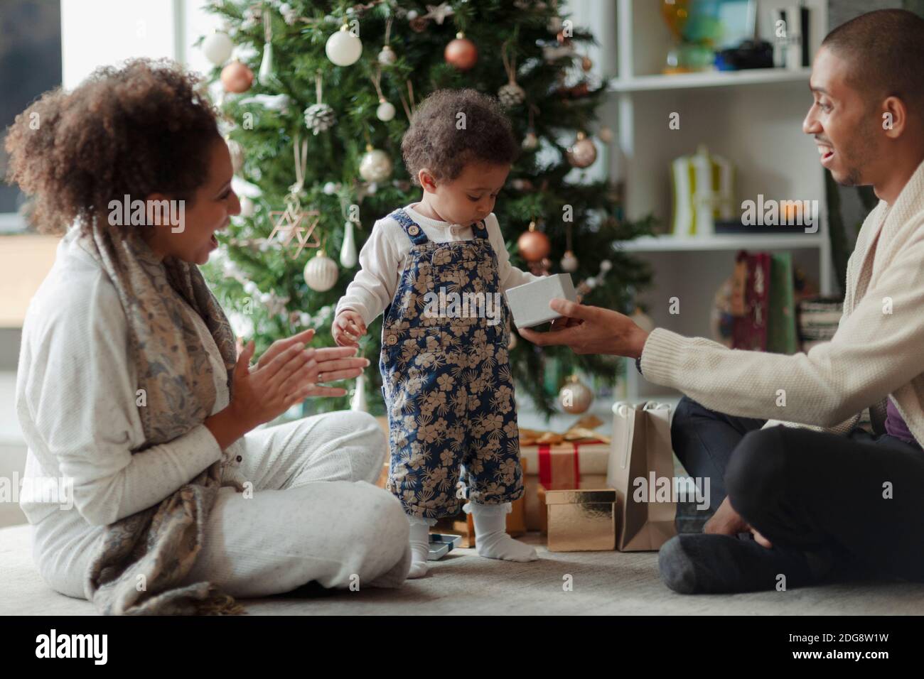 Glückliche Eltern und Baby Tochter Eröffnung Weihnachtsgeschenk von Baum Stockfoto