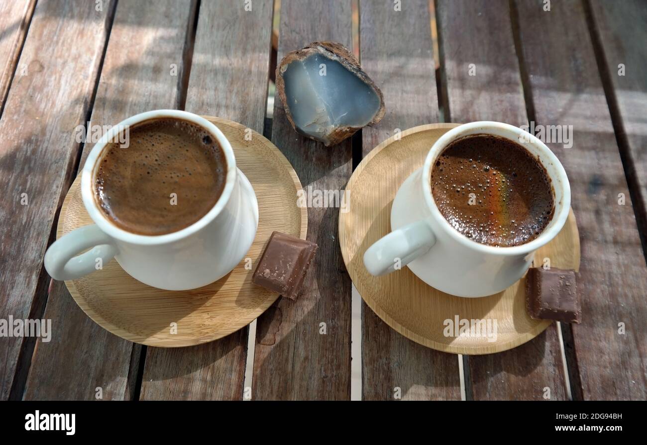Schäumender türkischer Kaffee aus frisch gerösteten und fein gemahlenen Kaffeebohnen, serviert in kleinen Keramikbechern auf Bambusplatten mit Bitterschokolade-Stücken Stockfoto