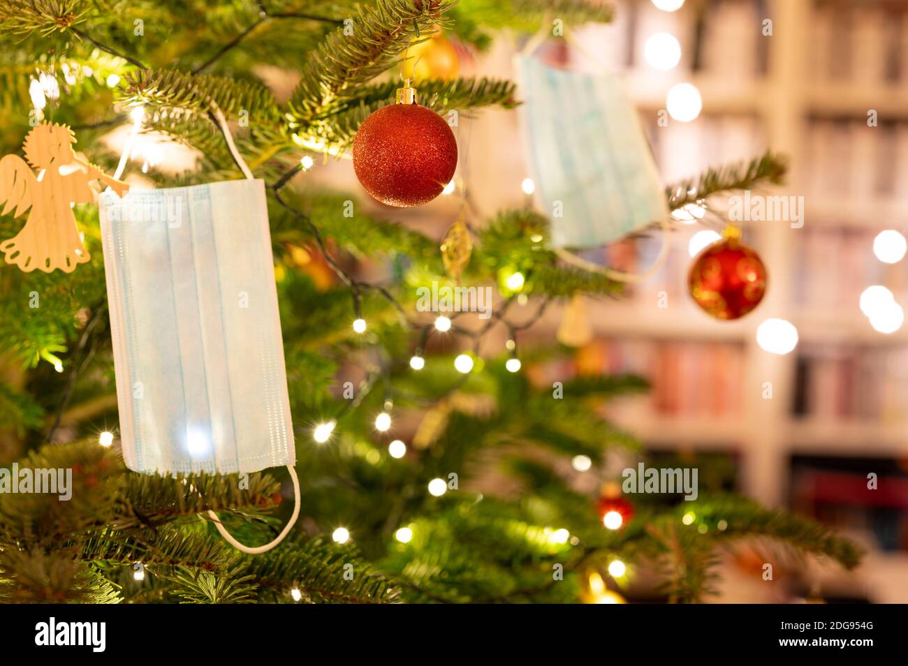 Gesichtsmasken hängen in einem schönen Weihnachtsbaum. Symbol für Weihnachtsfeiern während der Corona-Pandemie. Stockfoto