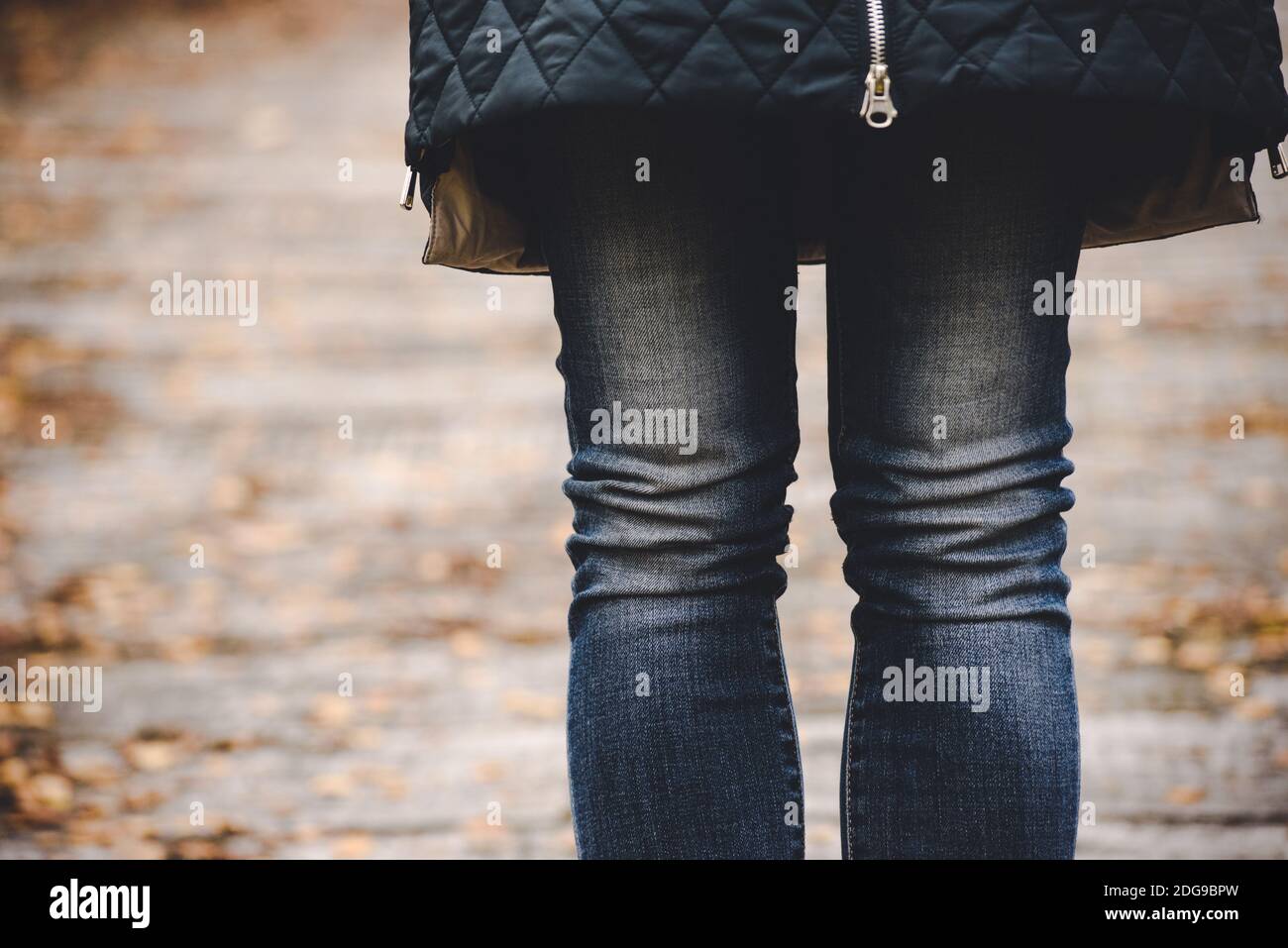 Dünne weibliche Beine in blauen Jeans vor dem Hintergrund Eine herbstliche Landschaft Stockfoto
