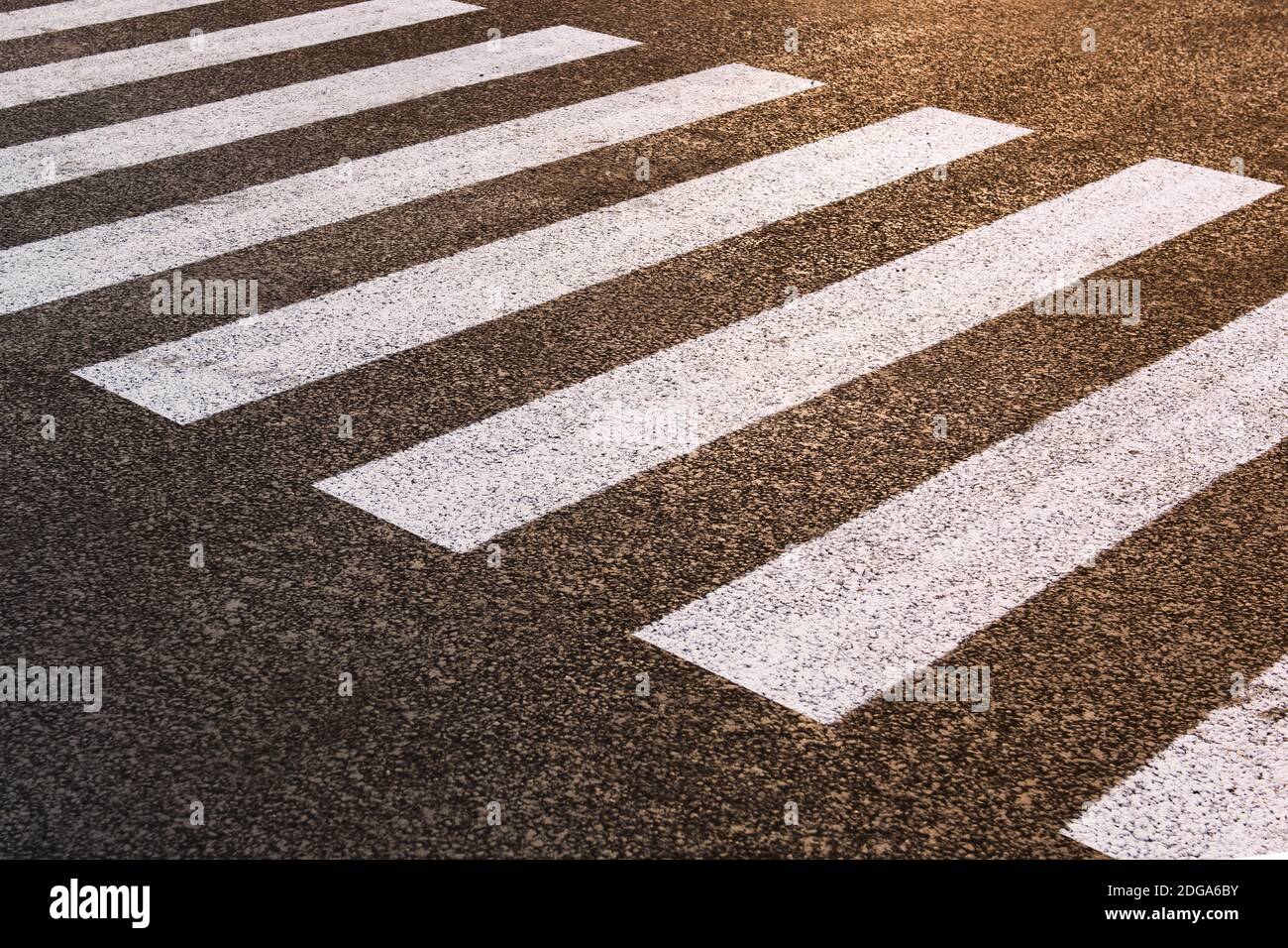 Ein leerer Fußgängerüberweg auf einer neuen Straße. Der Straßendienst zeichnete die Markierungen. Sonnenuntergangsgradient. Horizontales Foto. Stockfoto