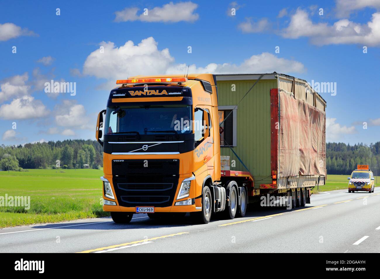 Yellow Volvo FH LKW-Sattelanhänger Rantala transportiert tragbare Kabine als Übergröße Last, Begleitfahrzeug folgt. Jokioinen, Finnland. Juni 15, 2020. Stockfoto