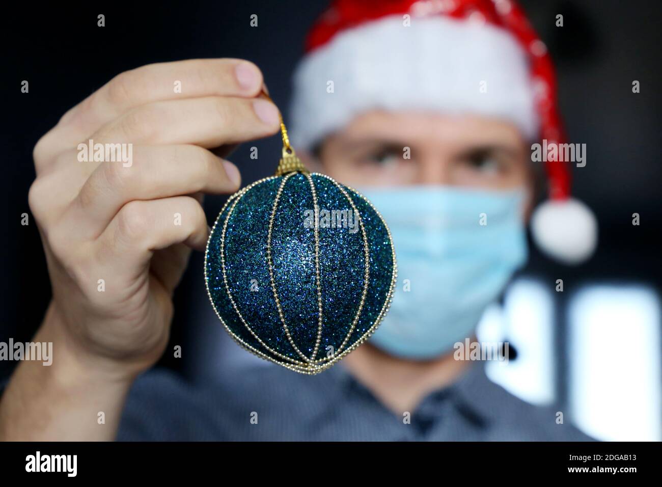 Weihnachtsfeier, Mann in Maske und Weihnachtsmann Hut mit einem blauen Spielzeugball in der Hand. Konzept der Heim- oder Bürodekoration für den Neujahrsurlaub Stockfoto