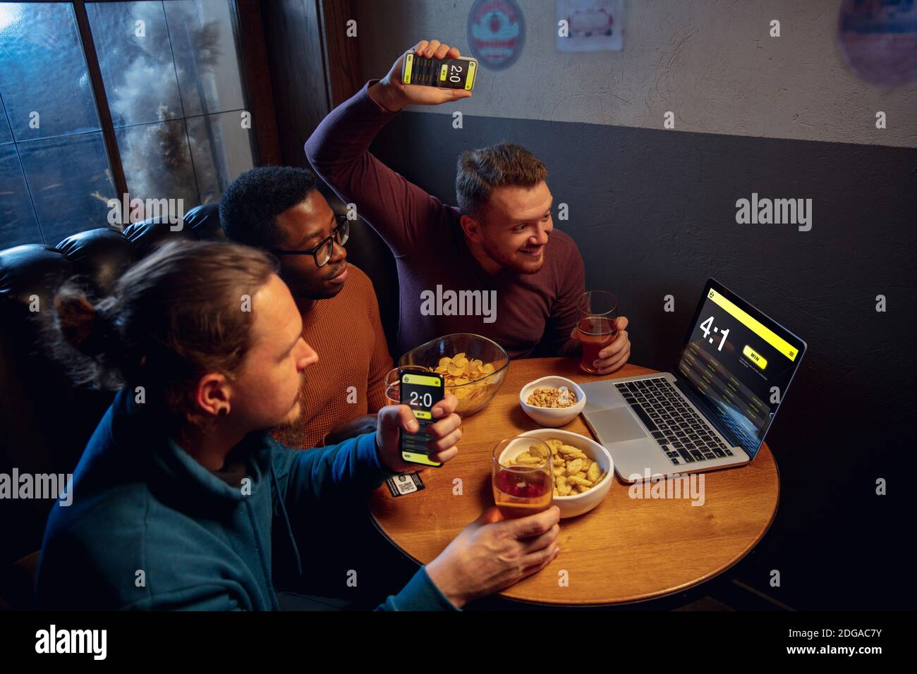 Analysieren. Begeisterte Fans in der Bar mit Bier und mobile App für Wetten, Punkten auf ihren Geräten. Bildschirm mit Match-Ergebnissen, emotionale Freunde jubeln. Glücksspiel, Sport, Finanzen, modernes techn Konzept. Stockfoto