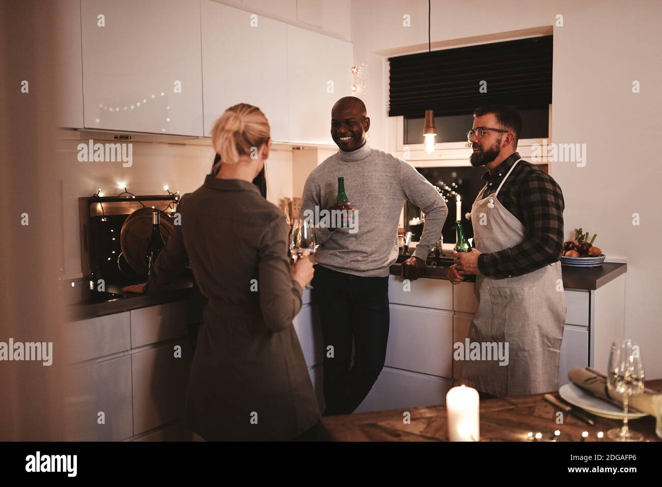 Eine Gruppe lächelnder Freunde, die in einer Küche miteinander sprechen Bei einem Drink vor einer Abendparty Stockfoto