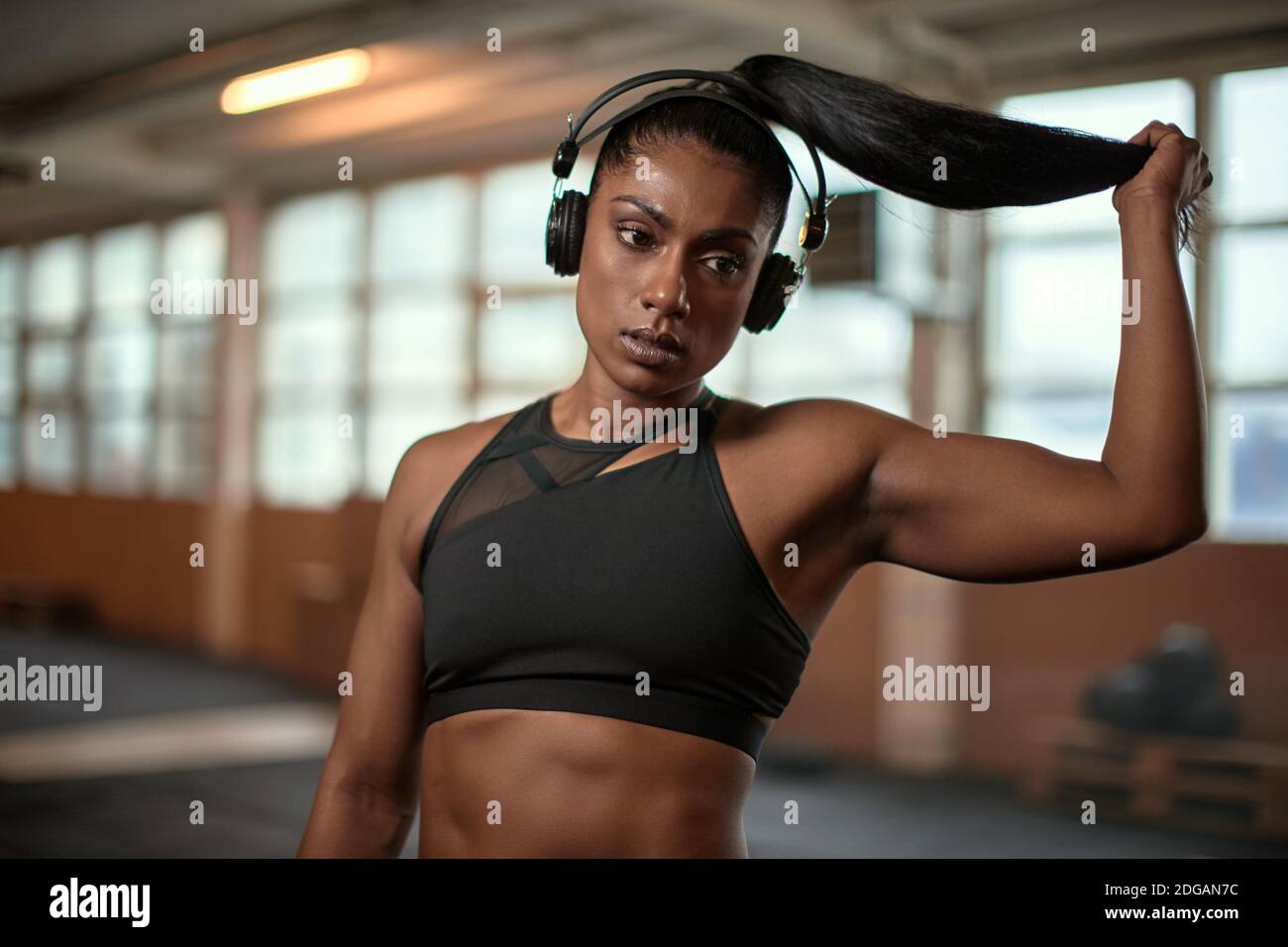 Ethnische Athletin schaut weg und zieht Pferdeschwanz beim Zuhören Zur Musik in der Pause im Training in der modernen Turnhalle Stockfoto