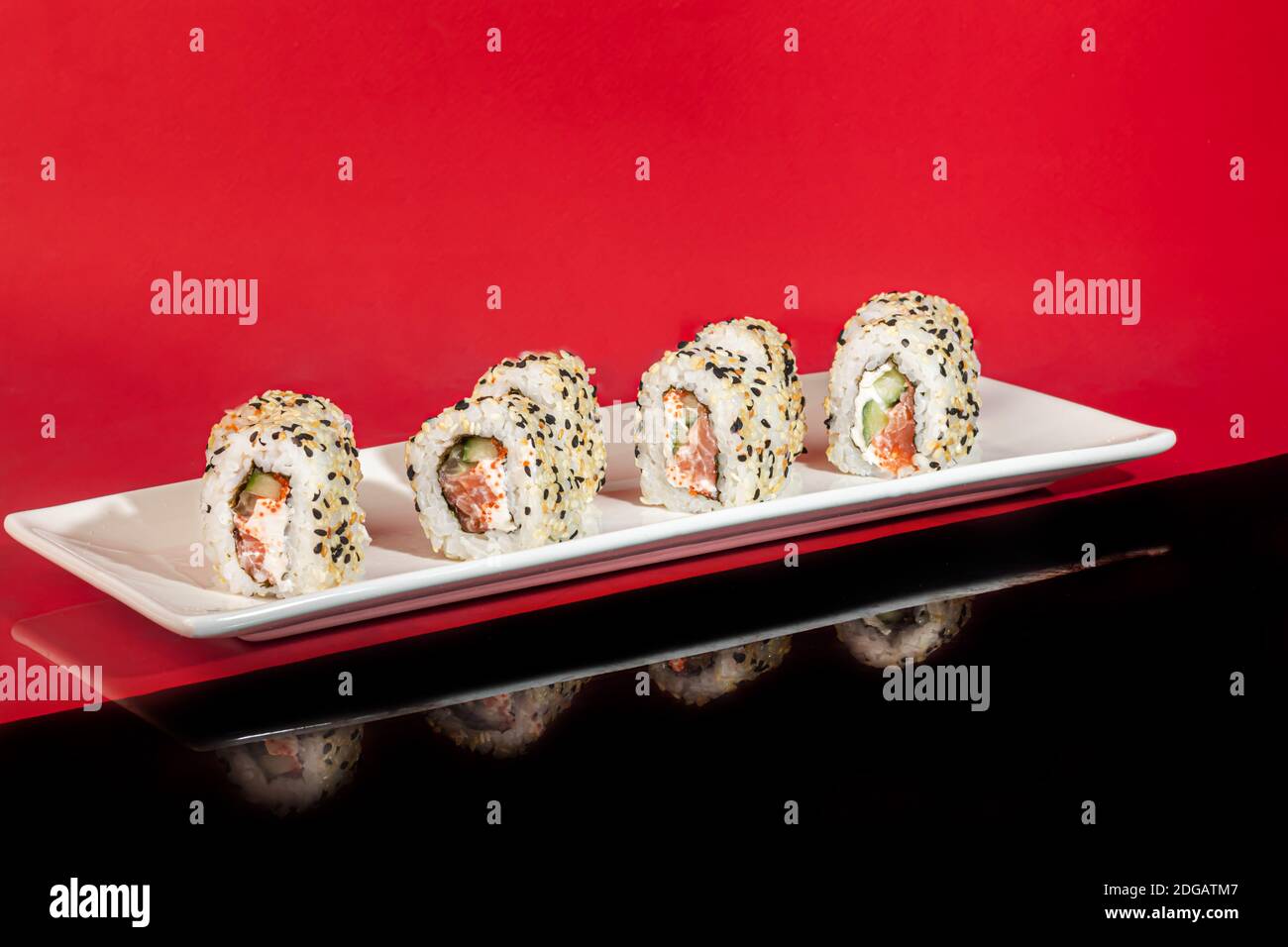 Sushi setzt Nigiri, Uramaki, California, Philadelphia, auf einen weißen Teller. Auf einem roten Hintergrund. Speicherplatz kopieren. Stockfoto