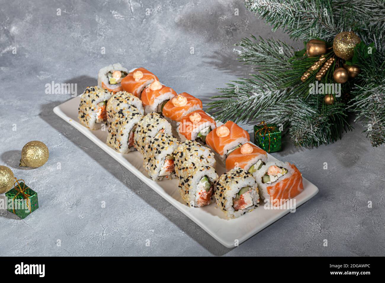 Sushi setzt Uramaki, California, Philadelphia, auf einen weißen Teller. Neujahr und festliches Konzept. Auf einem hellgrauen Hintergrund. Speicherplatz kopieren. Stockfoto