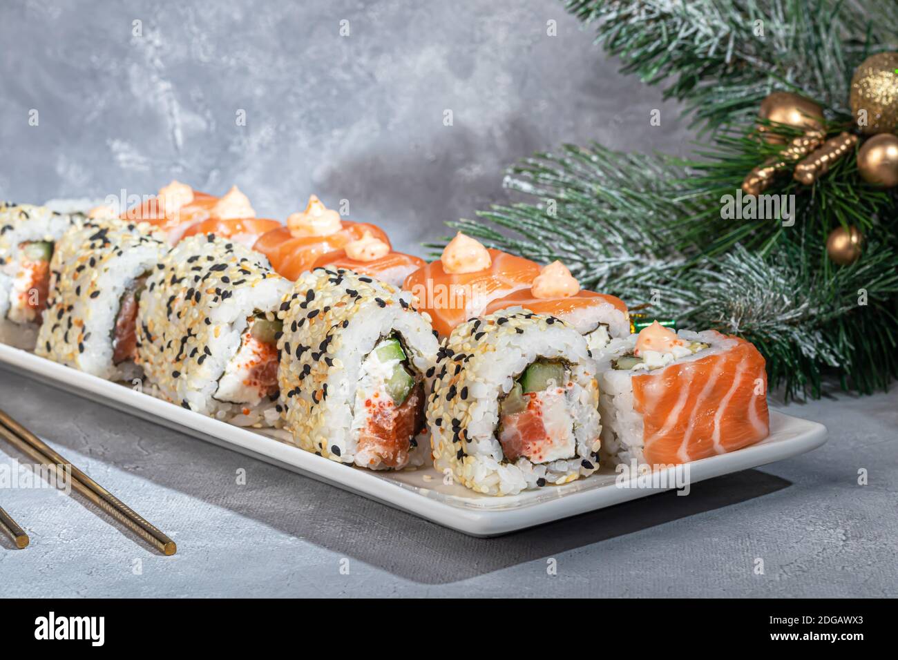 Sushi setzt Uramaki, California, Philadelphia, auf einen weißen Teller. Neujahr und festliches Konzept. Auf einem hellgrauen Hintergrund. Speicherplatz kopieren. Stockfoto