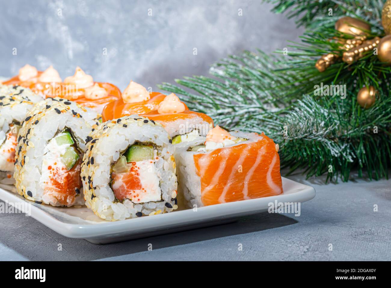 Sushi setzt Uramaki, California, Philadelphia, auf einen weißen Teller. Neujahr und festliches Konzept. Auf einem hellgrauen Hintergrund. Speicherplatz kopieren. Stockfoto