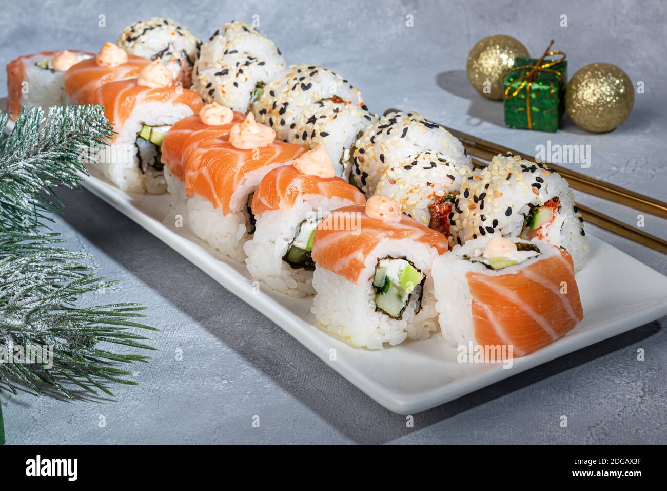 Sushi setzt Uramaki, California, Philadelphia, auf einen weißen Teller. Neujahr und festliches Konzept. Auf einem hellgrauen Hintergrund. Speicherplatz kopieren. Stockfoto