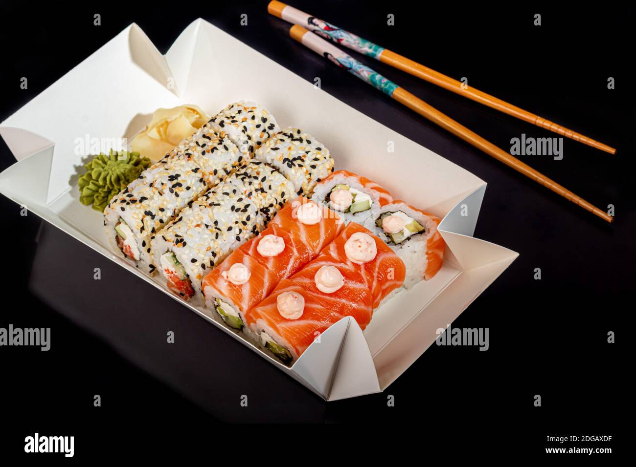 Sushi setzt Uramaki, California, Philadelphia, auf einen weißen Teller. Festliches Neujahrskonzept. Vor einem dunklen reflektierenden Hintergrund. Speicherplatz kopieren Stockfoto
