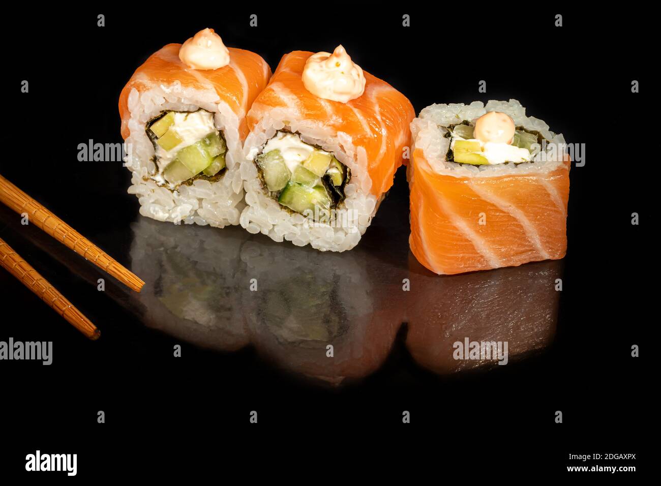 Sushi setzt Uramaki, California, Philadelphia, auf einen weißen Teller. Festliches Neujahrskonzept. Vor einem dunklen reflektierenden Hintergrund. Speicherplatz kopieren Stockfoto