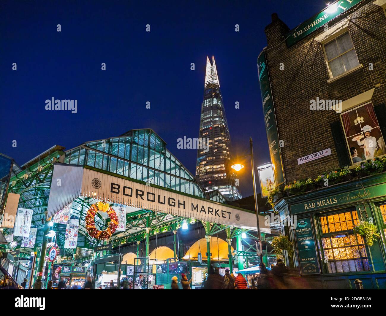 Borough Market Weihnachten Außenfassade Eingang & Weihnachtseinkäufer, Lichter Nacht mit Weihnachtskränze London Shard Tower hinter Southwark London UK Stockfoto