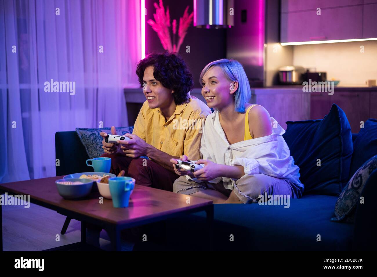 Glückliche junge Leute spielen Videospiele auf der Konsole, während sie auf der Couch vor dem fernseher sitzen. Millennial paar verbringen Spaß Zeit zusammen zu Hause. Zimmer Stockfoto