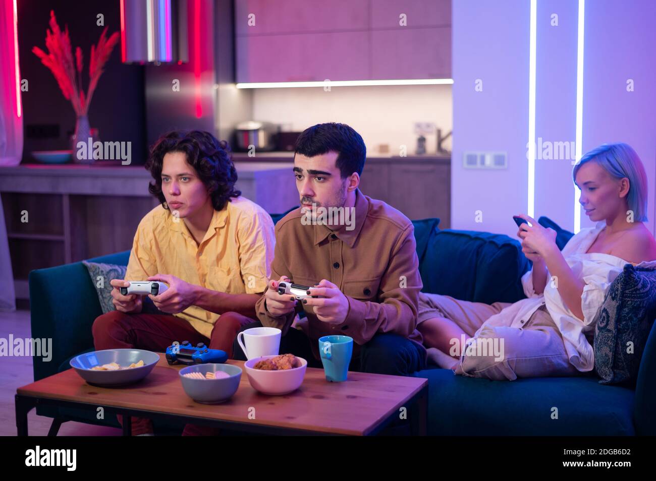 Jungs spielen Videospiel, während Mädchen mit Smartphone für soziale Medien. Freunde verbringen Zeit zusammen zu Hause. Stockfoto