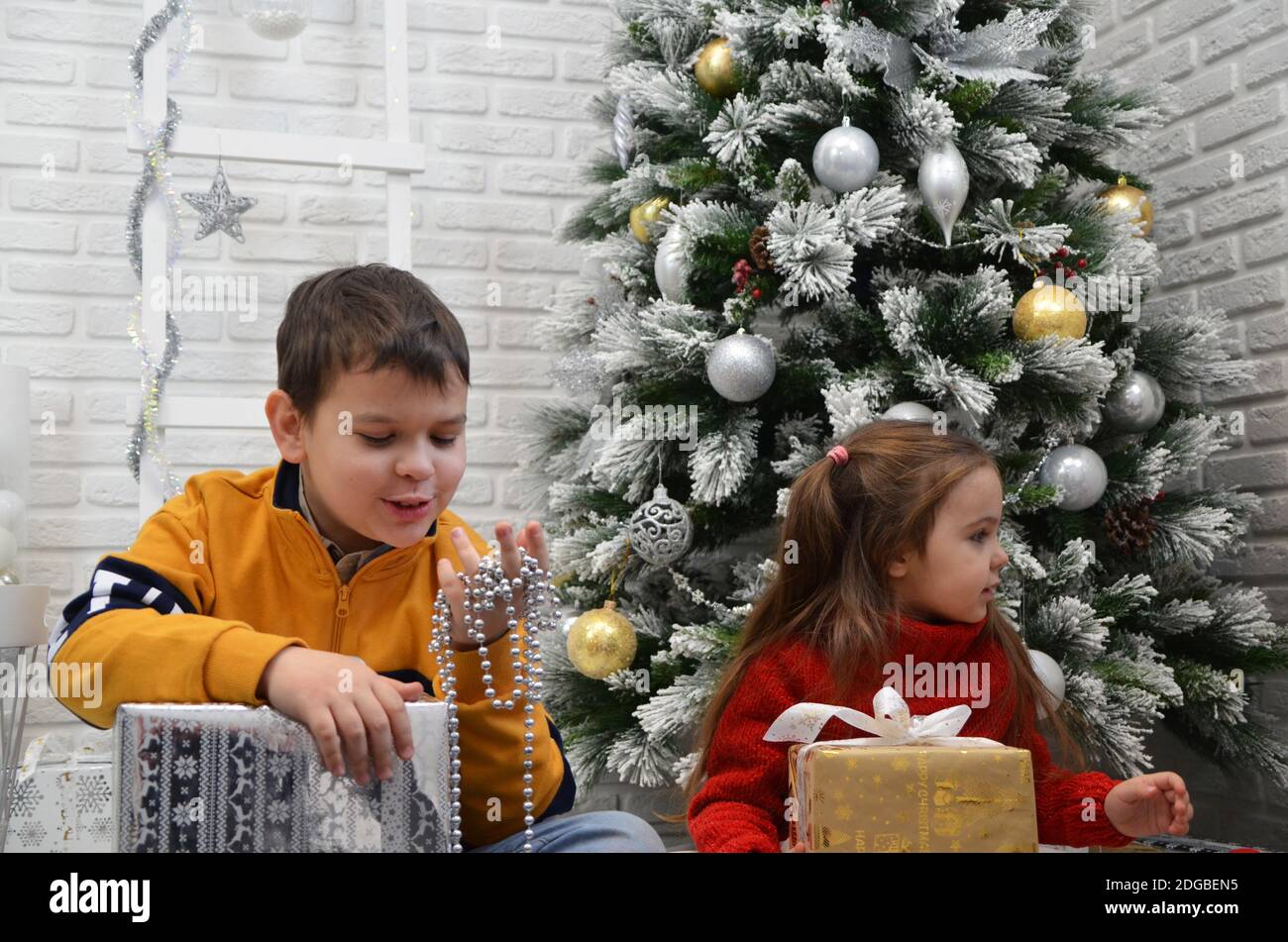 Glückliche kleine Kinder schmücken Weihnachtsbaum in schönen Wohnzimmer mit traditionellen Kamin. Kinder Eröffnung Geschenke am Weihnachtsabend. Offene Geschenke, pla Stockfoto