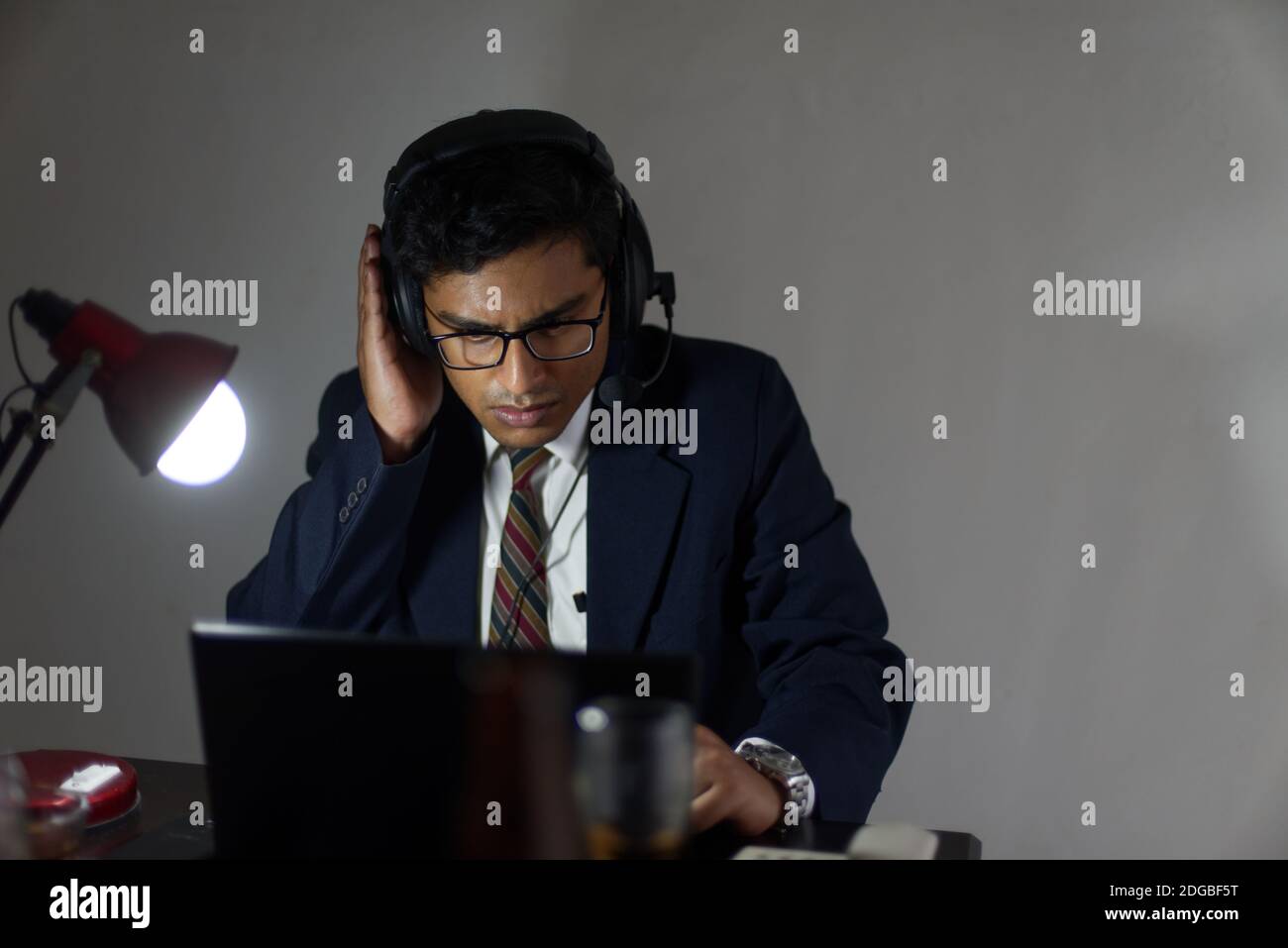 Ein indischer Bengali groß, dunkel, hübsch Brünette junge Mann / telecaller in Bürokleidung sitzt auf einem Bürotisch in Arbeitsstimmung im Büro Stockfoto