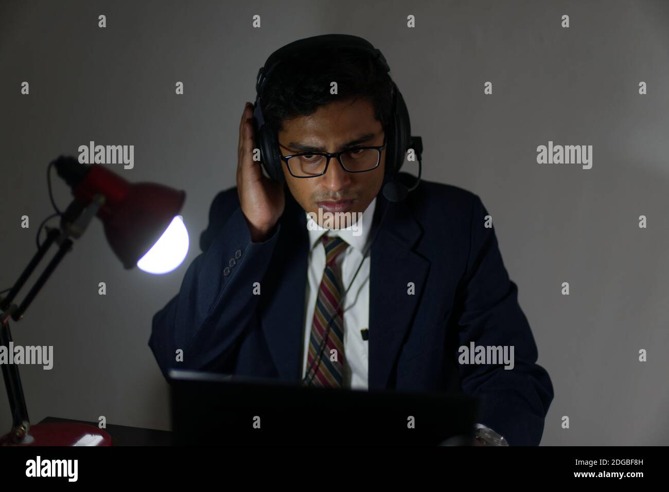 Ein indischer Bengali groß, dunkel, hübsch Brünette junge Mann / telecaller in Bürokleidung sitzt auf einem Bürotisch in Arbeitsstimmung im Büro Stockfoto