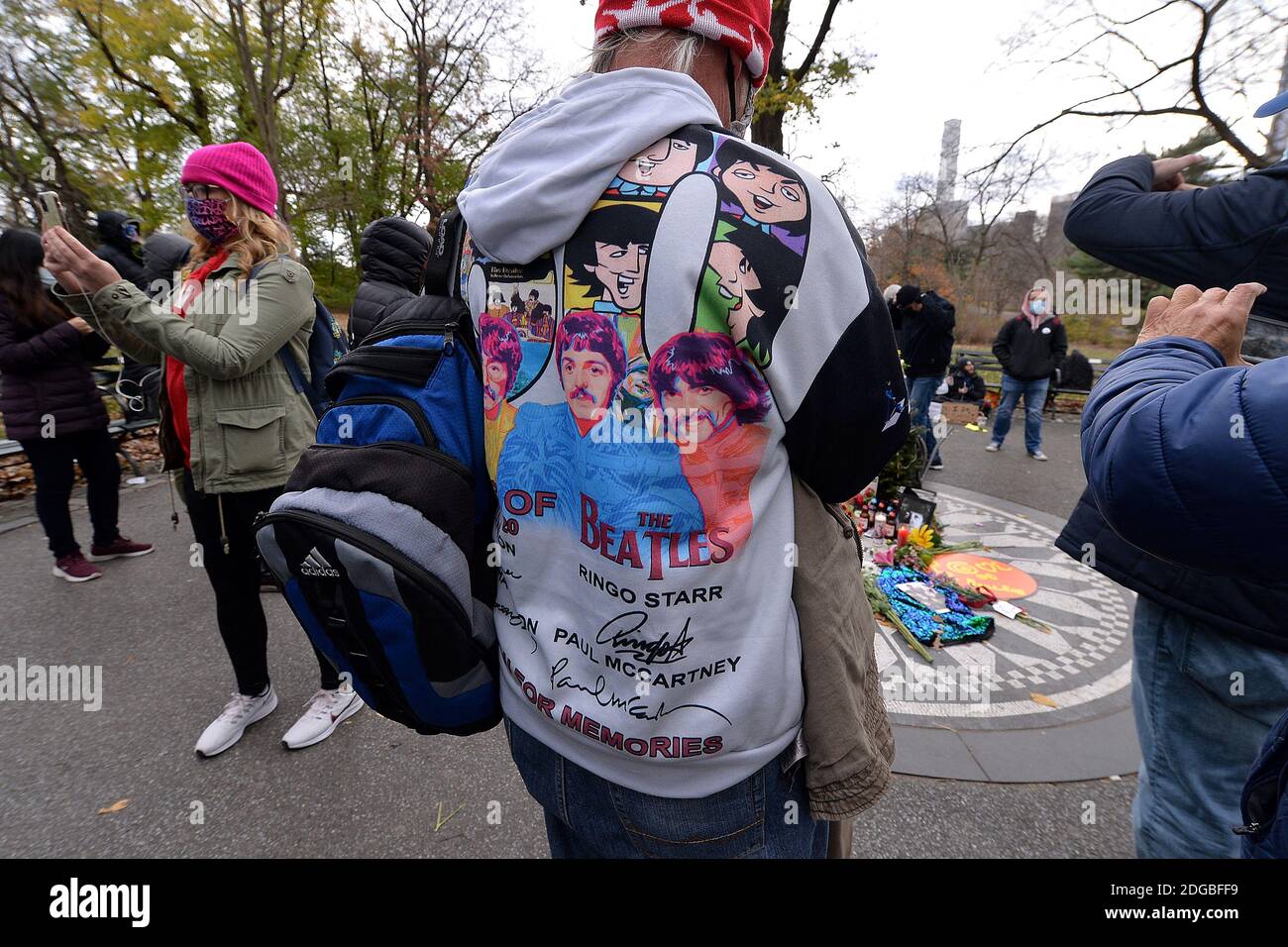 New York, USA. Dezember 2020. Ein Mann in einem Beatles-Hemd fotografiert Blumen und schmückt das Imagine-Mosaik in Strawberry Fields im Central Park, um an den 40. Todestag des Musikers John Lennon zu erinnern, New York, NY, 8. Dezember 2020. Der ehemalige Beatle wurde am Abend des 8. Dezember 1980 von einem Fan vor seiner Residenz The Dakota auf Manhattans Upper West Side erschossen. (Foto von Anthony Behar/Sipa USA) Quelle: SIPA USA/Alamy Live News Stockfoto