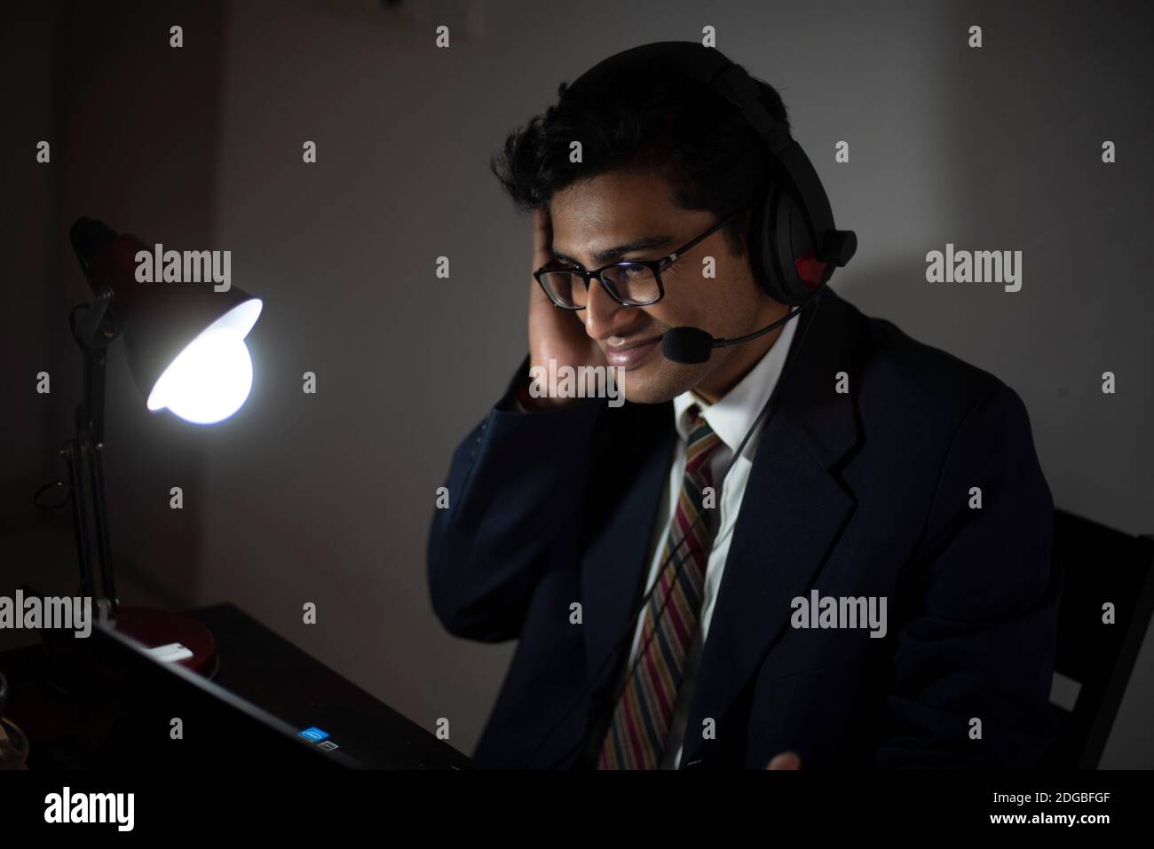 Ein indischer Bengali groß, dunkel, hübsch Brünette junge Mann / telecaller in Bürokleidung sitzt auf einem Bürotisch in Arbeitsstimmung im Büro Stockfoto