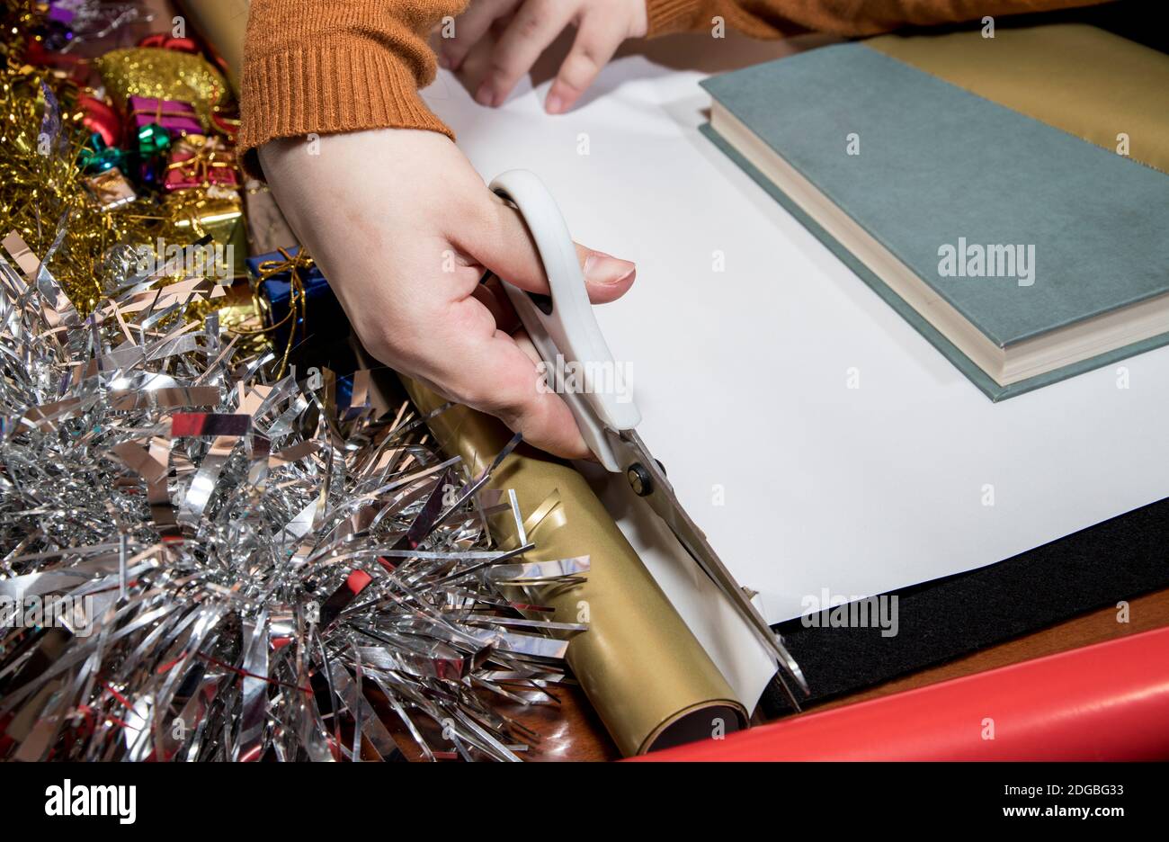 Junges Mädchen schneidet goldenes Geschenkpapier mit weißer Schere Auf einem Tisch mit schwarzem Hintergrund Stockfoto