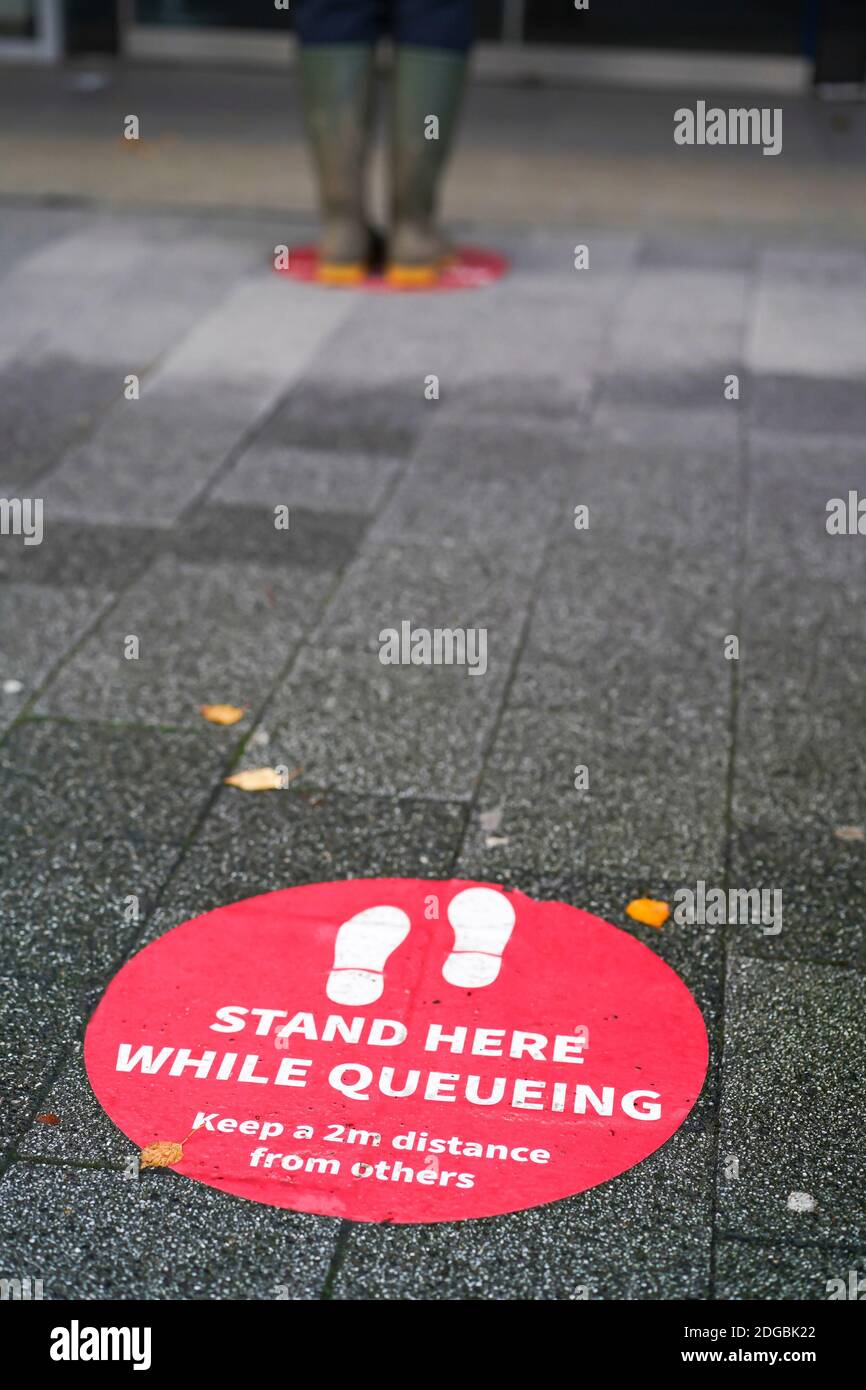 Soziale Wegmarkierungen auf dem Boden im Stadtzentrum von Großbritannien. Steht hier, während ihr ansteht. Halten Sie einen Abstand von 2 m zu anderen Personen ein. Stockfoto