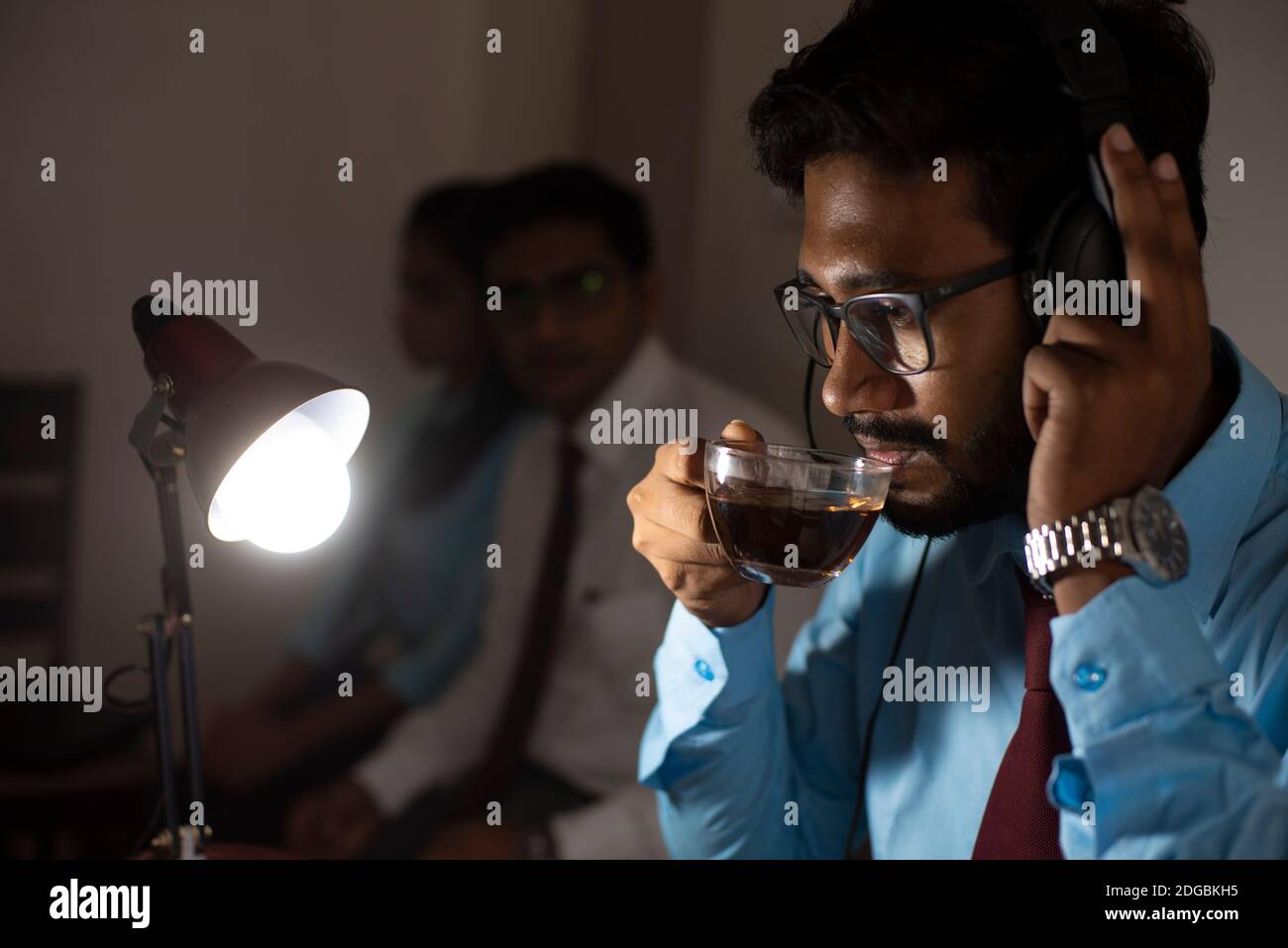 Ein indischer Bengali groß, dunkel, hübsch Brünette junge Mann / telecaller in Bürokleidung sitzt auf Bürotisch in Arbeitsstimmung in einem Büro Stockfoto