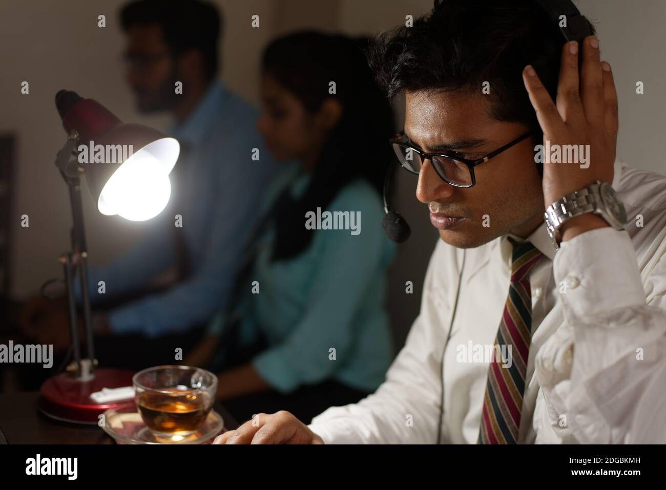 Ein indischer Bengali groß, dunkel, hübsch Brünette junge Mann / telecaller in Bürokleidung sitzt auf Bürotisch in Arbeitsstimmung in einem Büro Stockfoto