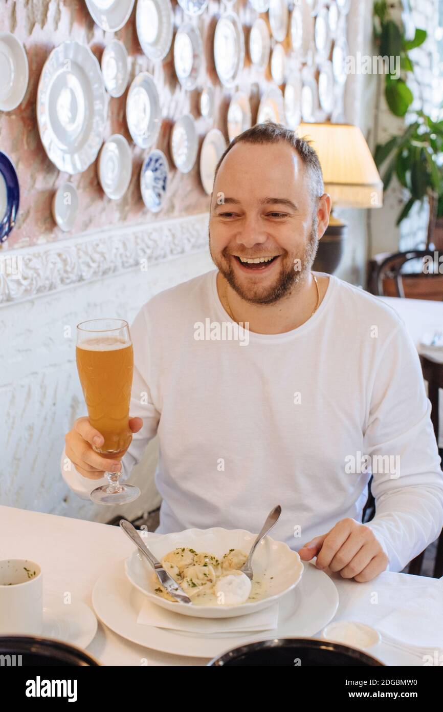 Lächelnder Mann, der in einem Restaurant sitzt, das Abendessen und Trinken isst Bier Stockfoto