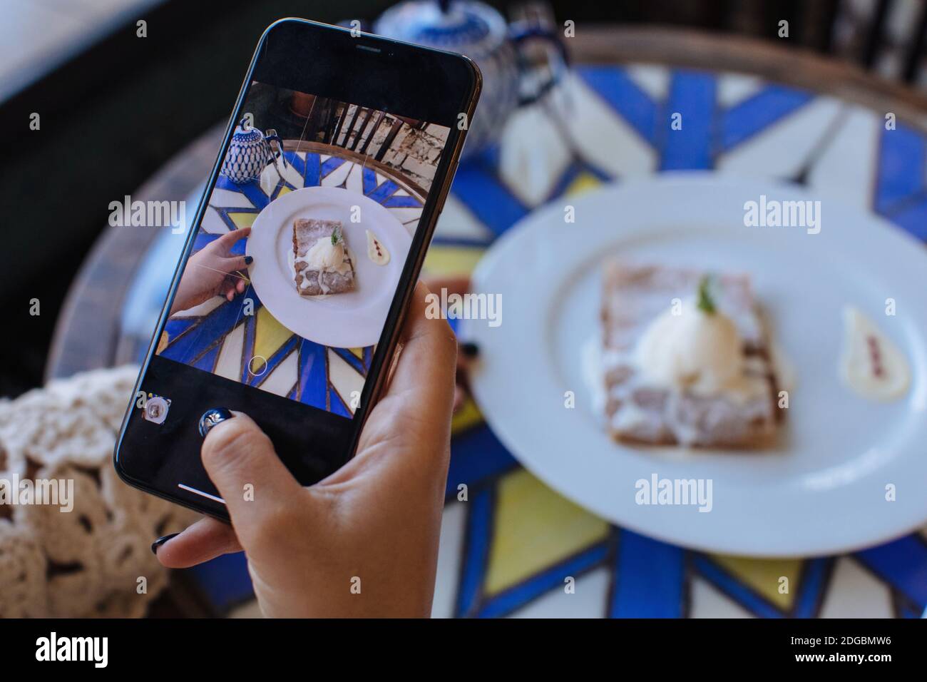 Frau, die in einem Café sitzt und ein Foto von Strudel fotografiert Mit Eis Stockfoto