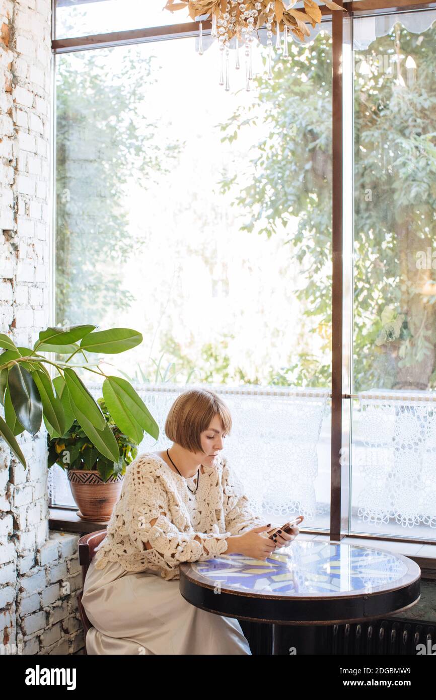 Frau, die in einem Café sitzt und ihr Mobiltelefon anschaut Stockfoto