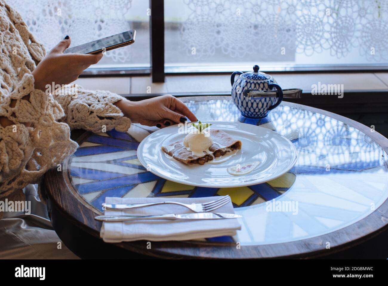 Frau, die in einem Café sitzt und ein Foto von Strudel fotografiert Mit Eis Stockfoto