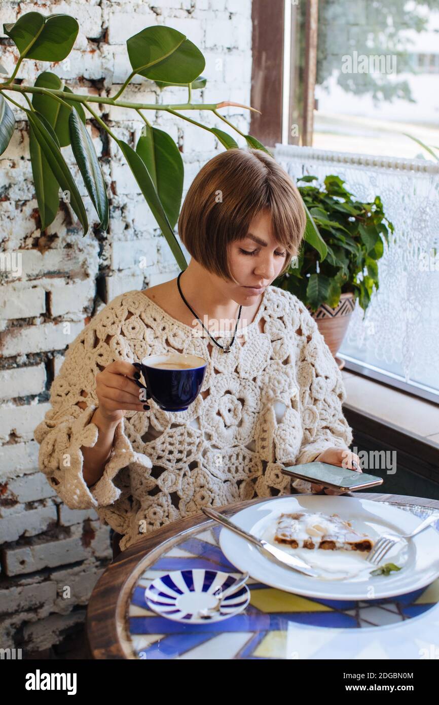 Frau, die in einem Café sitzt, Kaffee trinkt und anschaut Ihr Mobiltelefon Stockfoto