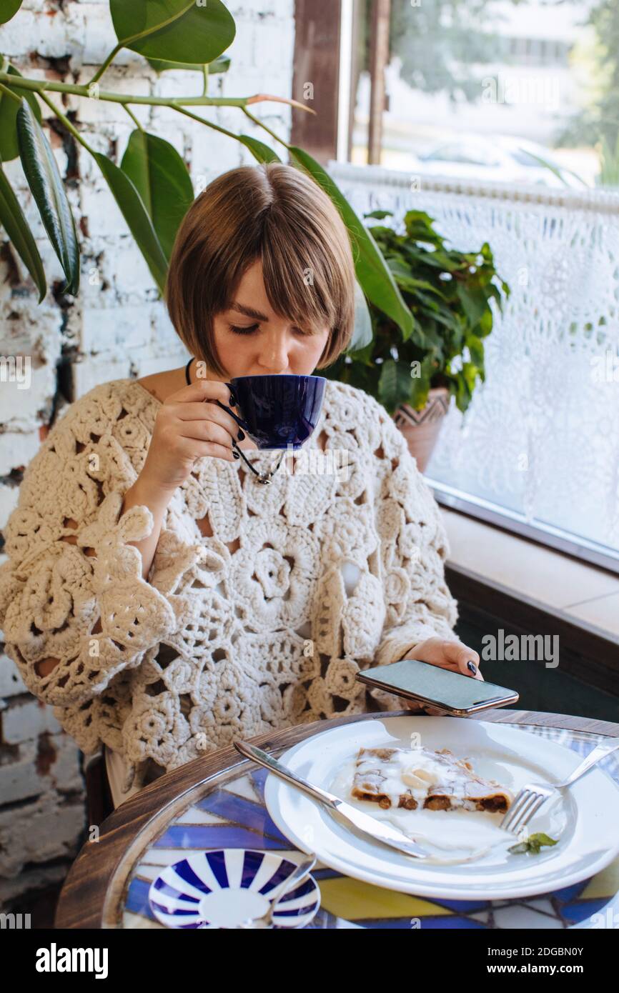 Frau, die in einem Café sitzt, Kaffee trinkt und anschaut Ihr Mobiltelefon Stockfoto